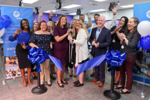 A celebratory ribbon-cutting ceremony features smiling community members and educators standing in front of a blue FPL banner, cheering and holding oversized scissors with a large blue ribbon stretched in front.
