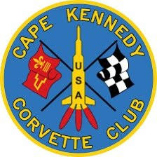 Round Cape Kennedy Corvette Club logo with a blue background, a yellow rocket labeled “USA” in the center, and crossed red and black racing flags behind it.