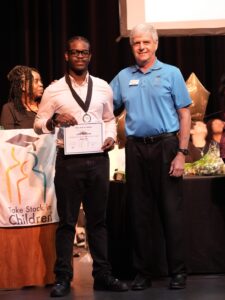 Take Stock in Children of Brevard scholar Leon Robinson stands with mentor Jim Clamons during a student recognition ceremony, highlighting the impact of mentorship on student success.